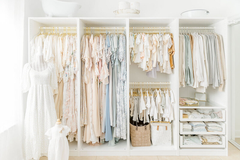An organized white wardrobe showcases a serene collection of pastel and white garments on hangers, perfect for a Destin FL family photography session. A mannequin displays a chic white dress, while storage baskets neatly occupy the lower shelves.