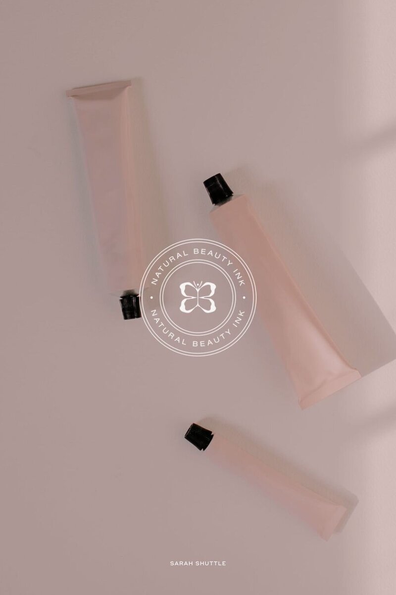 Submark with butterfly emblem over soft pink background photo for feminine permanent makeup branding.