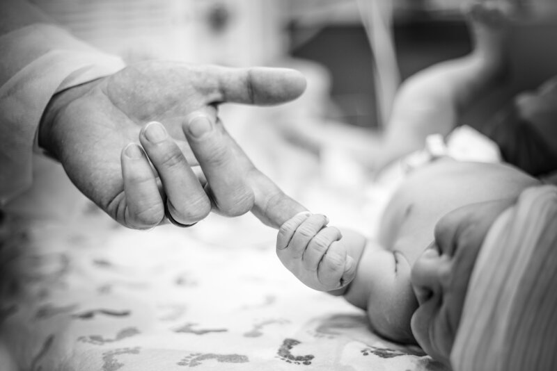 A new father and newborn hold hands