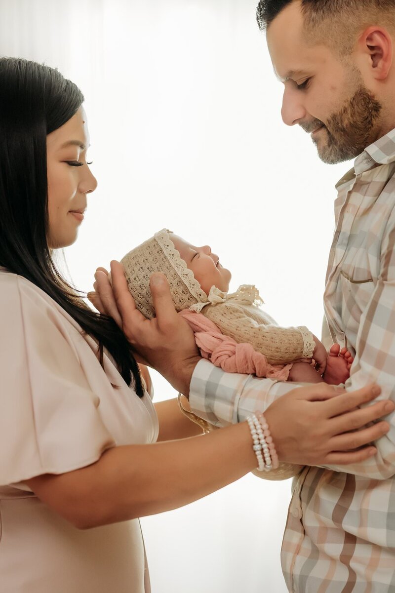 newborn girl between her parents. she is smiling as she sleeps
