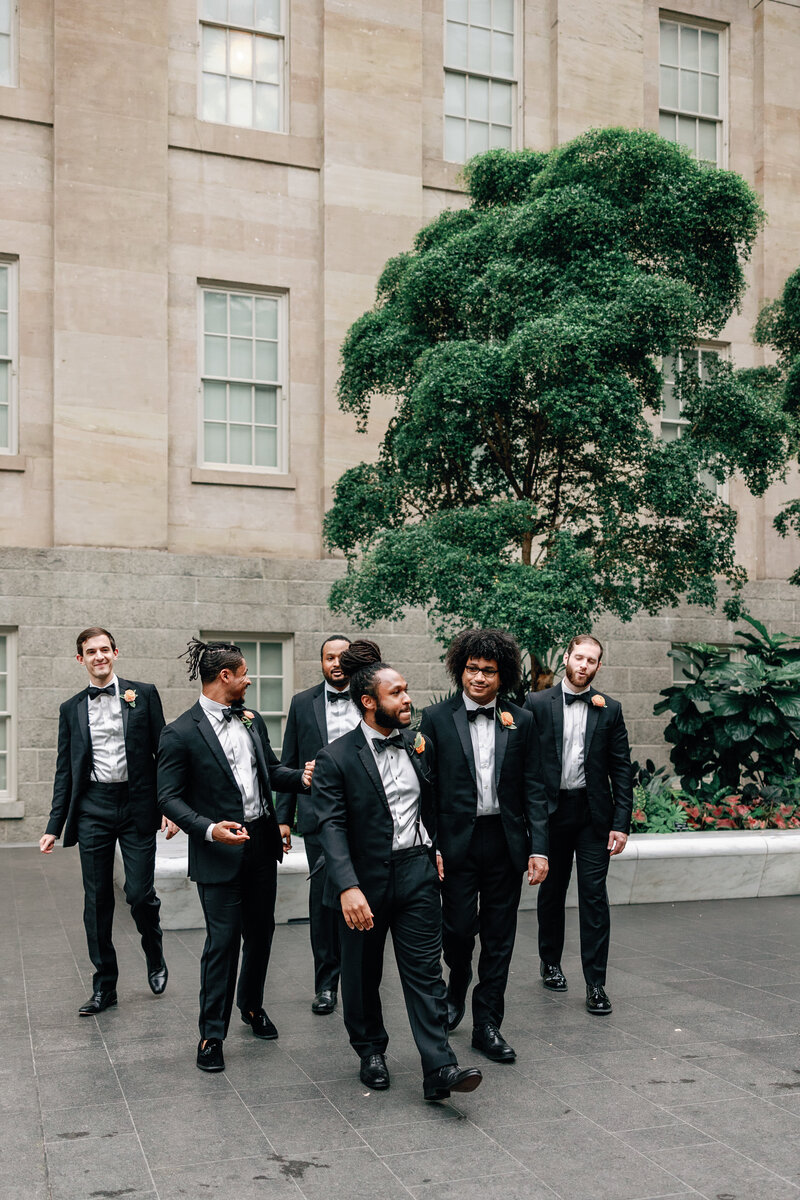 Groomsmen laugh as they are photographed inside the National gallery of Art in a classy fine art wedding in Washington DC