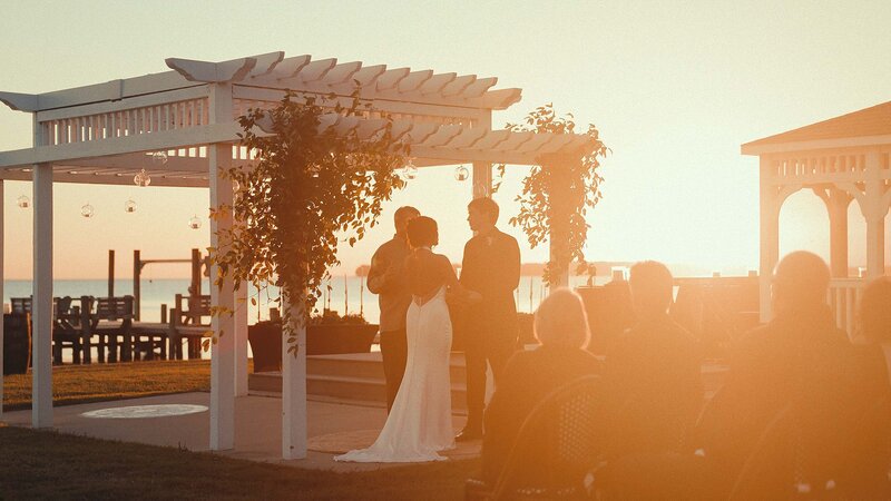 This wedding film frame grab from Films by Brian, a Williamsburg, VA-based destination wedding videographer, shows a beautiful bride and her groom at their sunset wedding ceremony on the water in North Carolina.