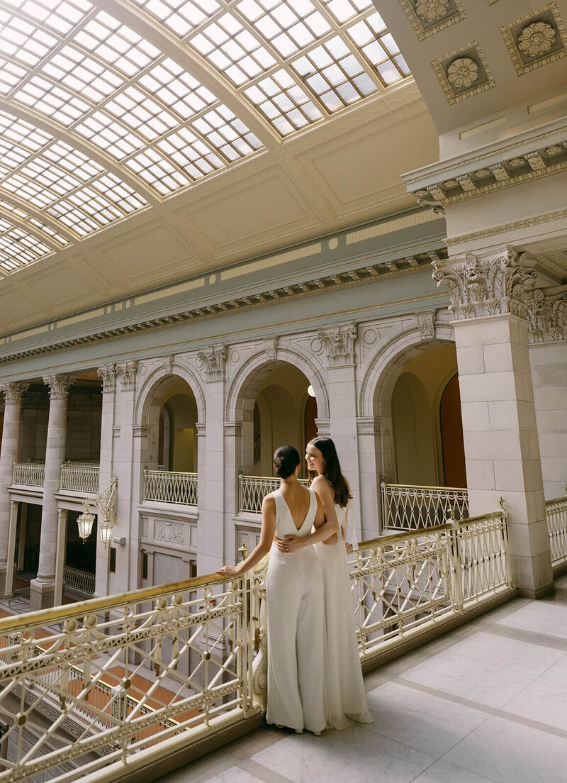 Bride's are hugging, looking at each other and smiling during the wedding session at the City Hall
