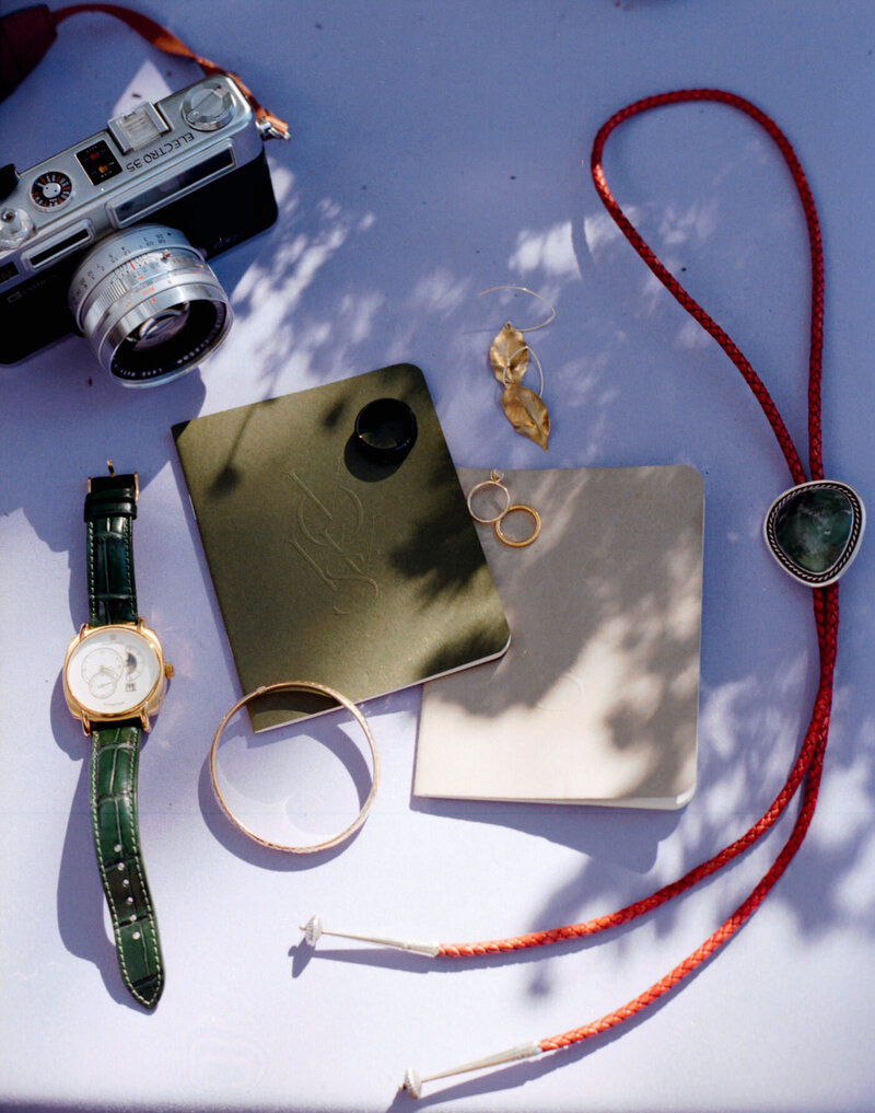 A collection of details photographed on film displaying vow books, wedding rings and jewewlyry, and a film camera