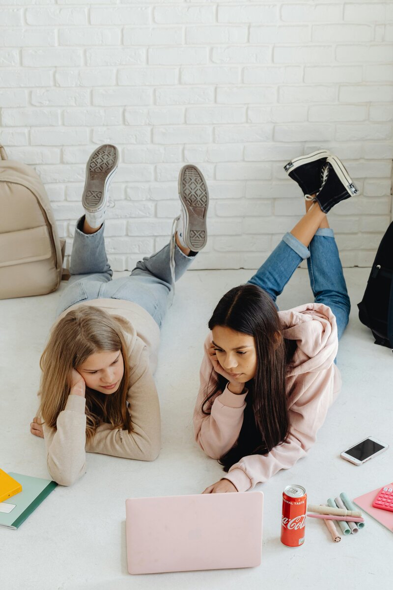 deux adolescentes qui sont couchées sur le ventre en regardant un ordinateur portable