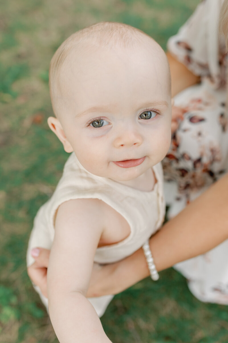 A sweet outdoor portrait of a baby gazing into the camera while being held by their mother in High Park, Toronto. The warm, natural light and lush greenery create a timeless and emotive moment, reflecting the deep bond between mother and child. Captured by KCP Families.
