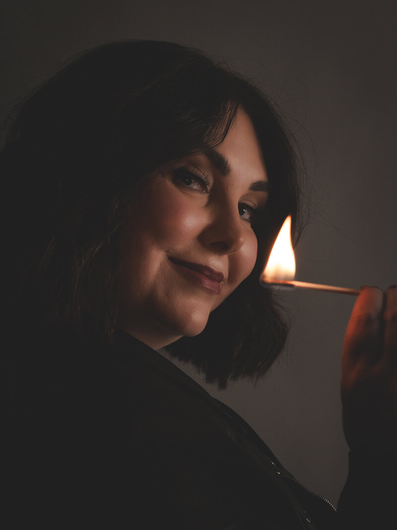 Founder of ByeCurious, poses with a lit match to symbolize igniting your power and burning down what no longer serves you.