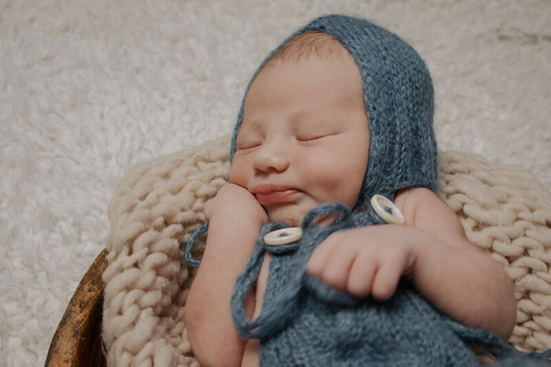 Newborn baby peacefully sleeping, wearing a knitted blue outfit and bonnet