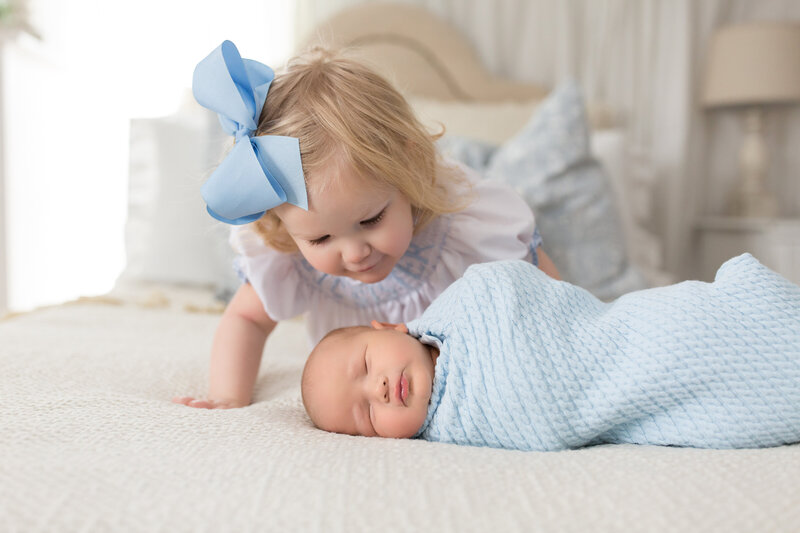 Big sister watching new baby on bed