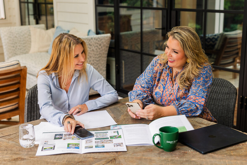 realtor women team wearing wearing coordinated outfits working at a patio table with paper, pen, brochures and one talking to each other during branding with Laure Photography Atlanta