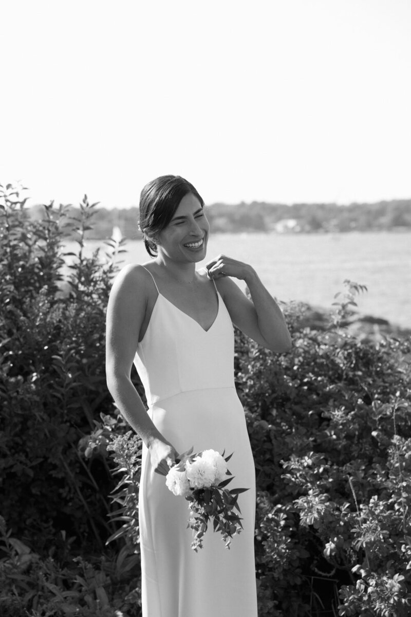 Smiling bride holding a bouquet, standing by greenery.