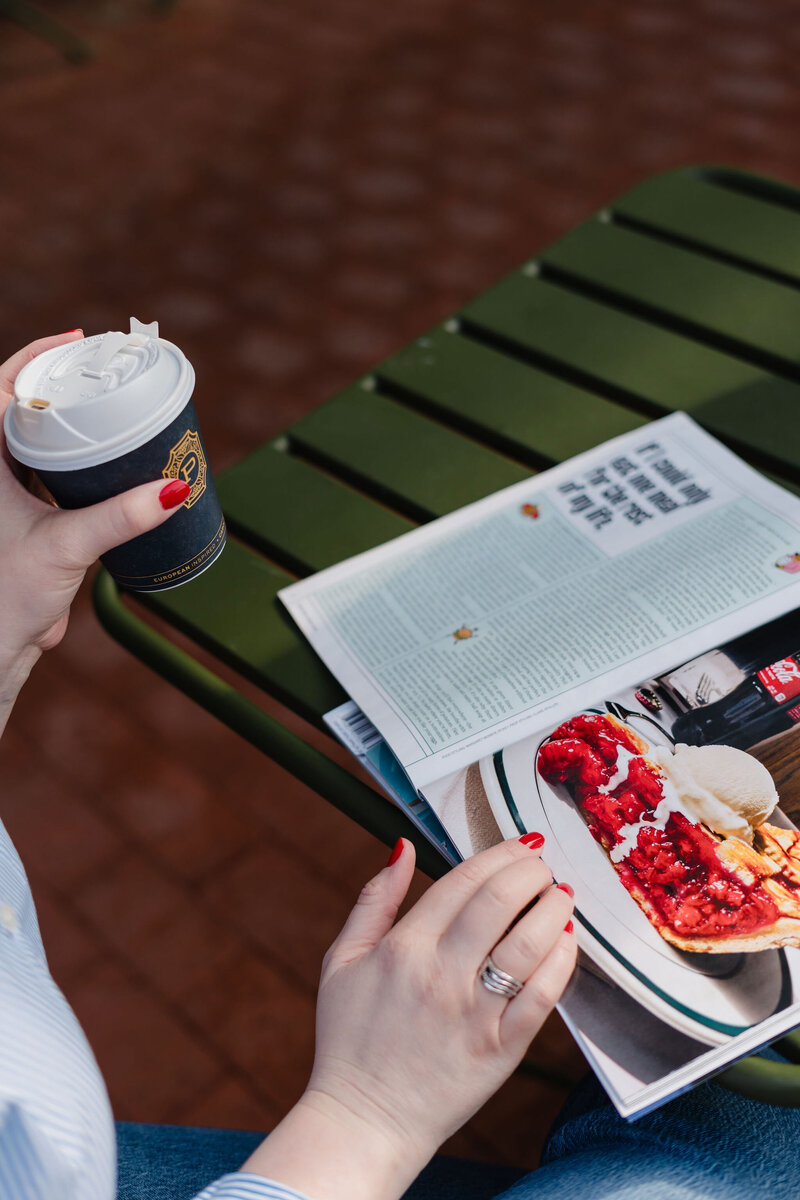 Anna Bradshaw copywriter flipping through a magazine and holding coffee at an outdoor coffee table