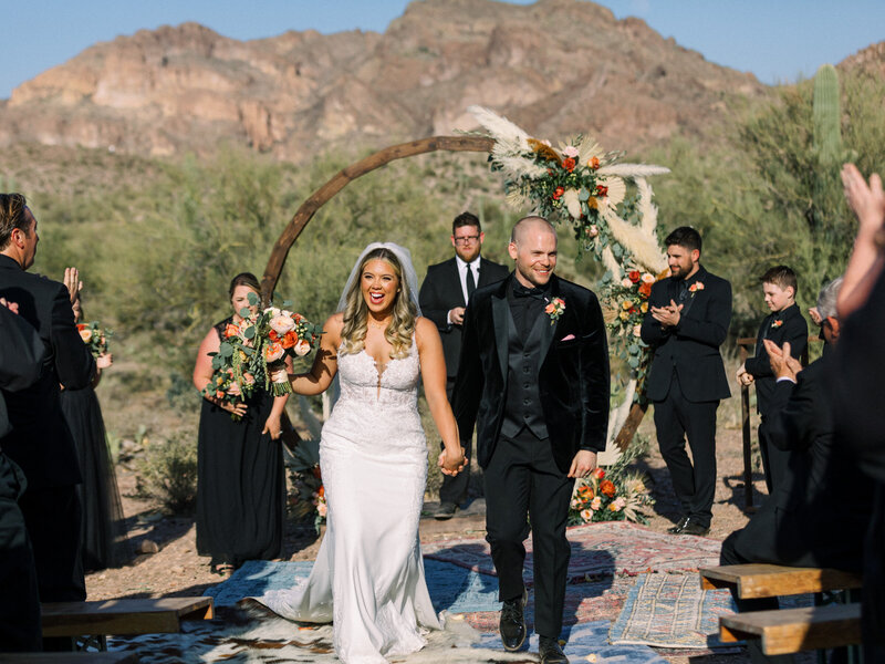 bride and groom holding hands while walking down the aisle