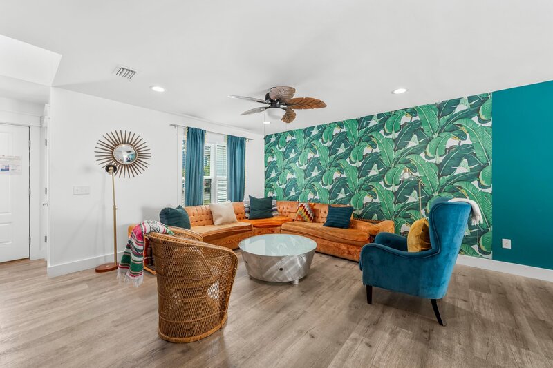 Eclectic lounge at Tropical House with cozy mid-century style couches, palm ceiling fan, and lively tropical wallpaper.