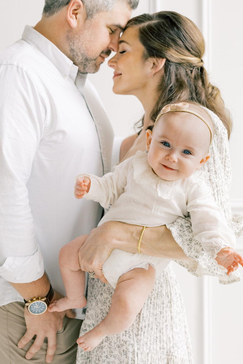 Cozy milestone session with parents cuddling baby in neutral-toned Charlotte studio, showcasing intimate family connection.