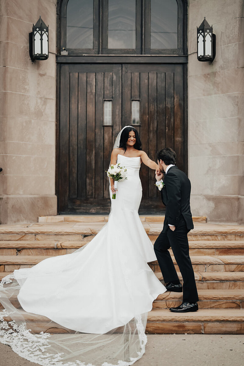 groom kisses smiling brides hand standing on stairs