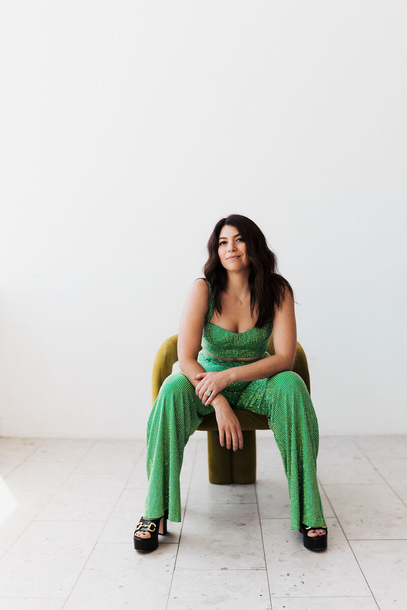 Sam wearing green jumpsuit sitting in chair