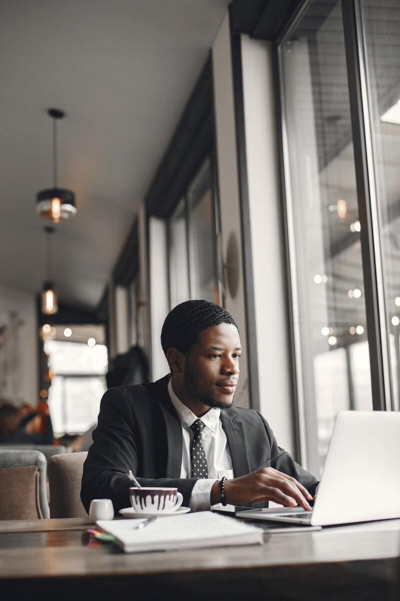 Thoughtful professional man in a suit working in a NYC cafe, representing ambitious clients seeking therapy at LightLine Therapy for stress, success pressure, and self-reflection.