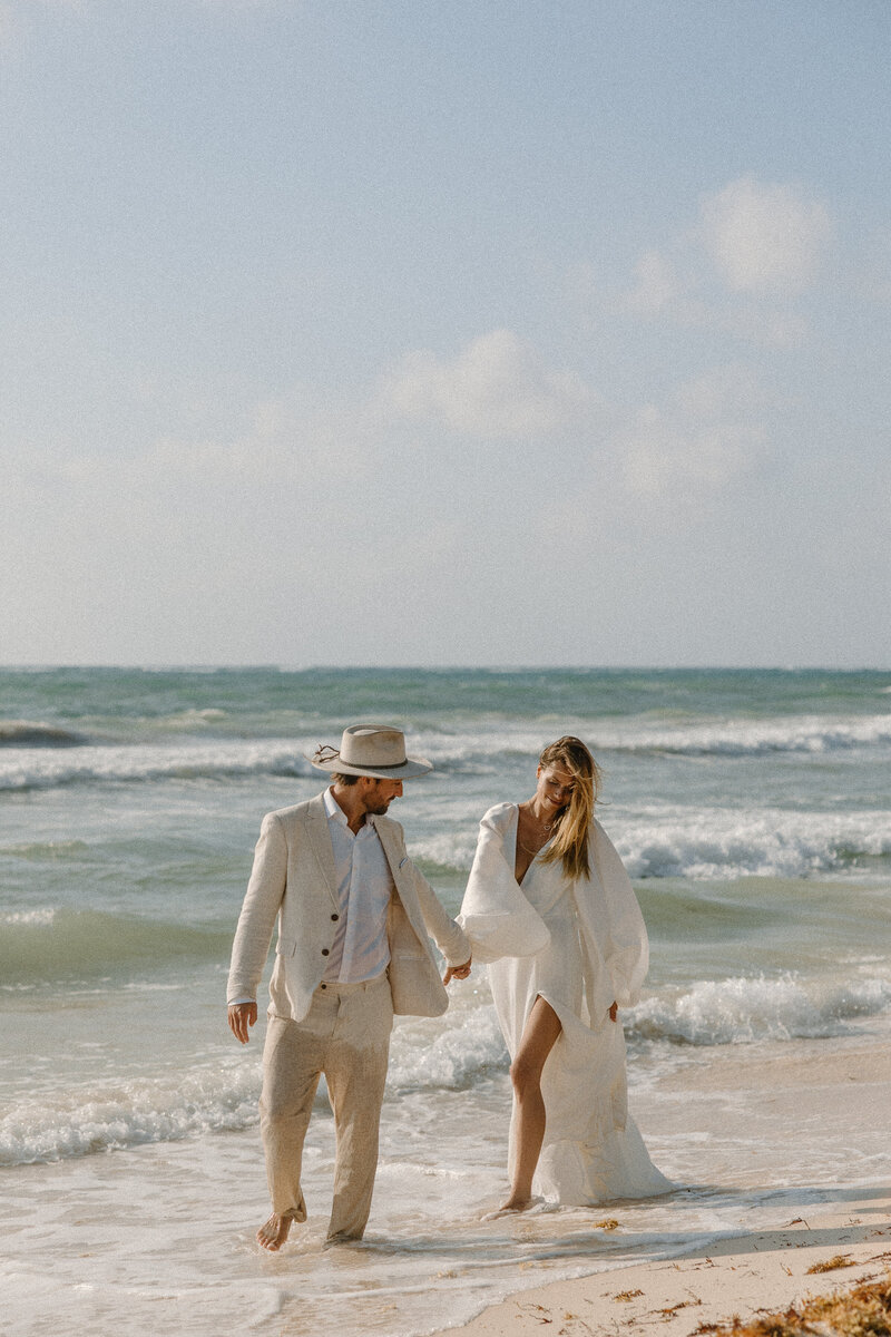 Couple walking hand in hand along the shoreline, waves crashing behind them during their Mexico beach elopement.