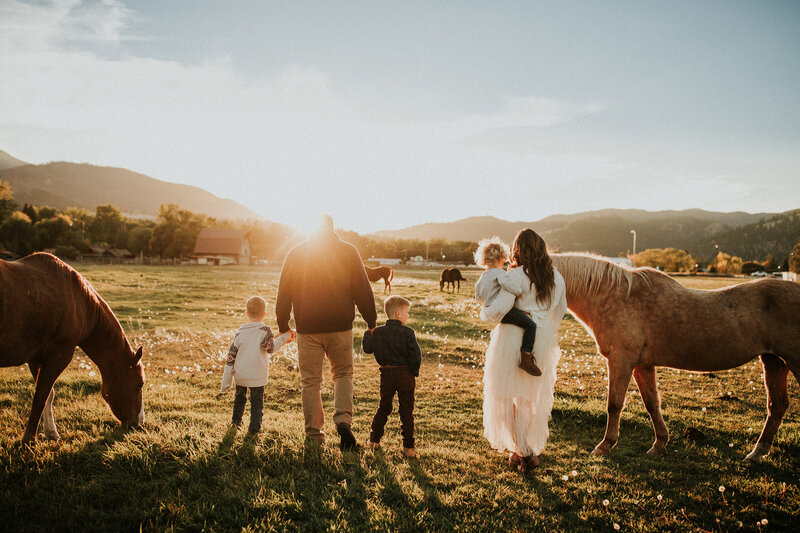 A family of five walking away on a ranch are in a horse pasture