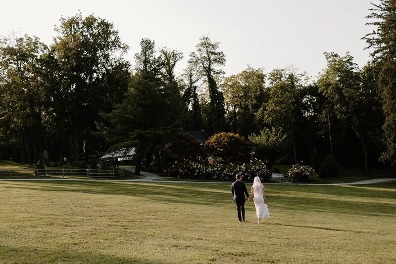A wedding couple holding hands and walking through a field. 