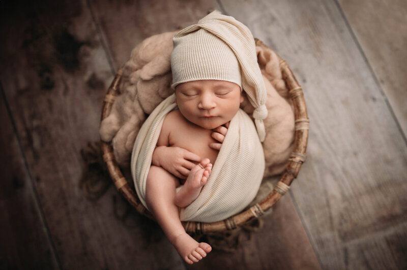New Haven CT Newborn photographer captures wrapped and posed newborn baby boy in beige hat and swaddle inside a round wooden bowl