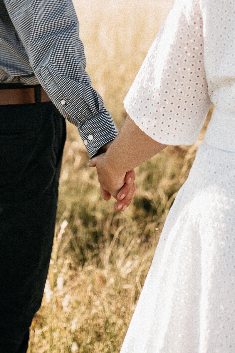 engaged couple walking through a field holding hands