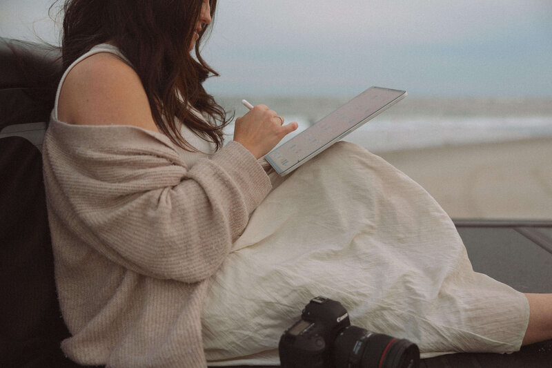 marissa a business coach is sitting down writing on an ipad next to a camera