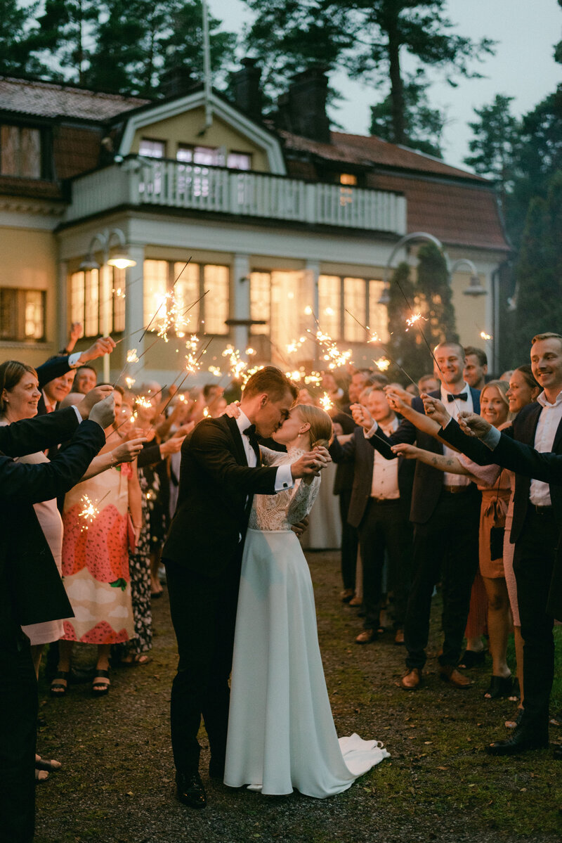 Documentary wedding photo of bride and groom and guests with sparkles in front of Airisniemi manor in Turku. A cheerful and romantic image by wedding photographer Hannika Gabrielsson.