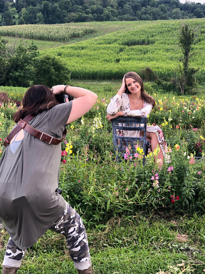 Photo shoot of senior girl sitting on blue chair in field of flowers