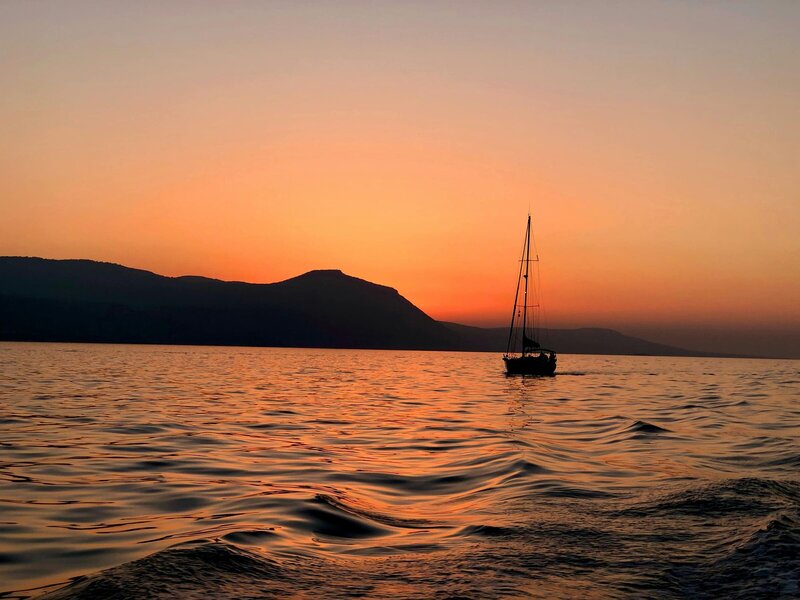 Segelyacht von oben auf dem Meer in tükisblauen Wasser und vier Menschen auf Luftmatratzen im Wasser