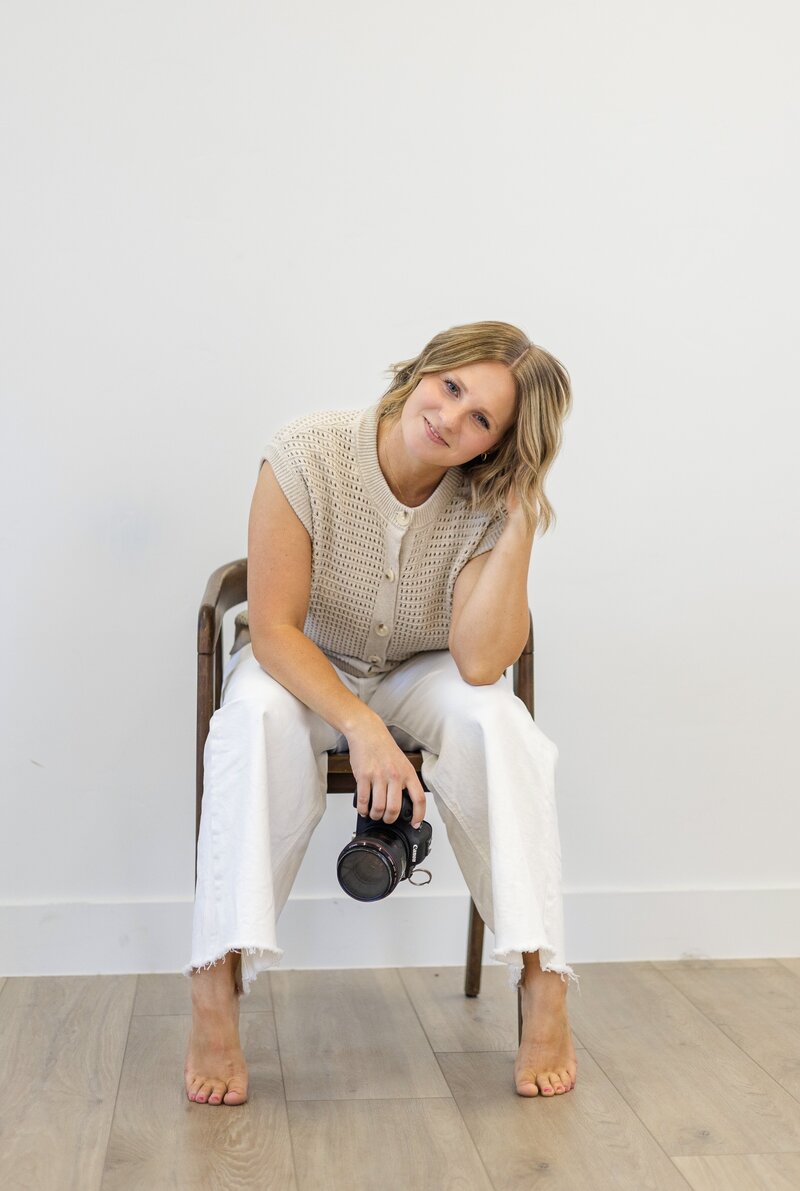 Extended family photographer sitting in a chair with camera and smiling 