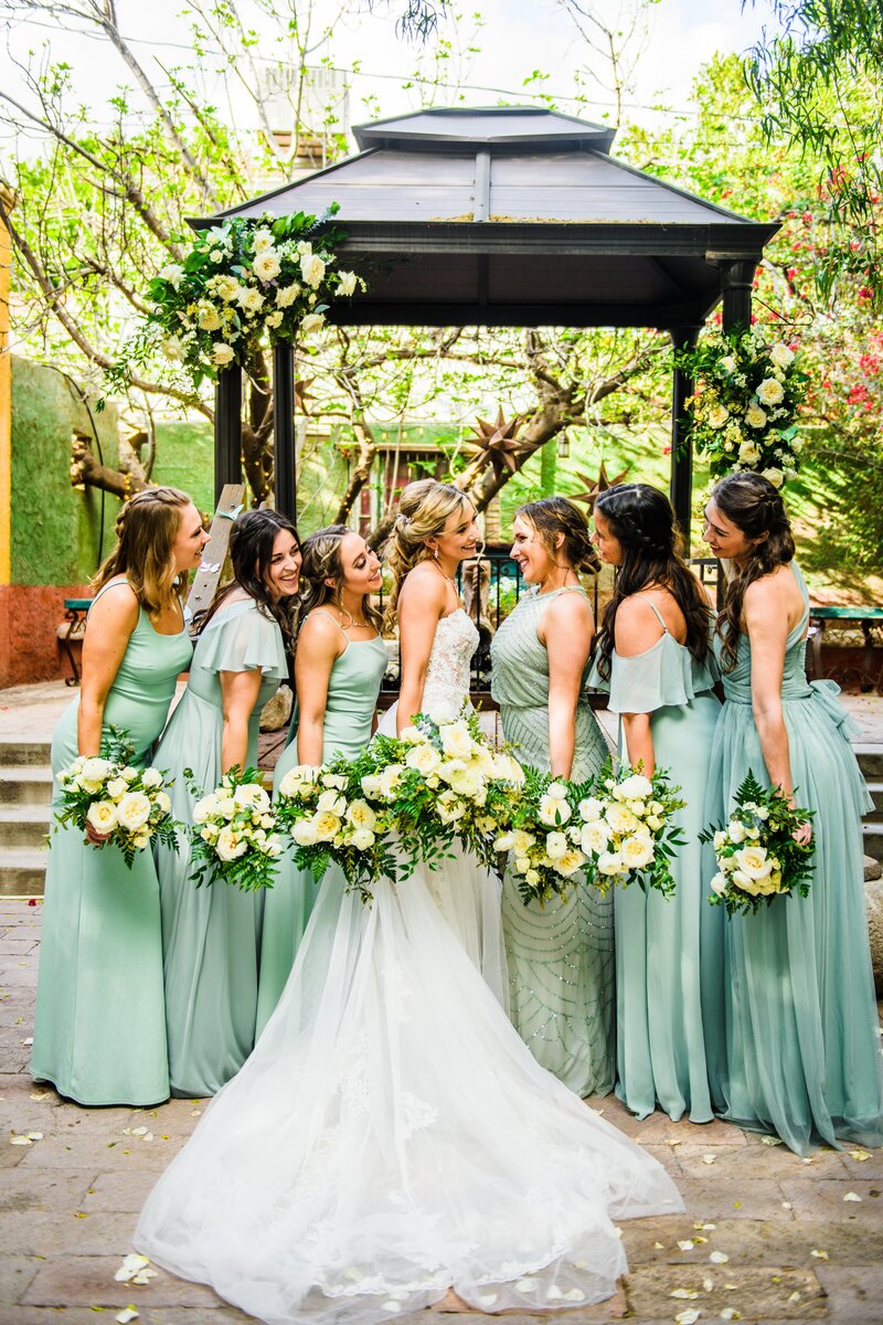 Bride smiling at Bridesmaids holding wedding bouquets in green dresses at Boojum Tree Hidden Gardens photography