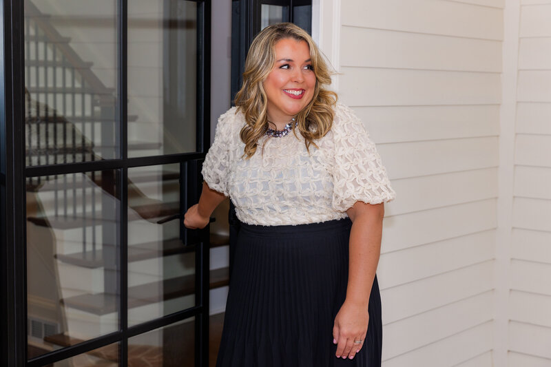 realtor woman wearing an off white blouse and a black skirt opening an Atlanta house modern front door and looking behind her during photoshoot