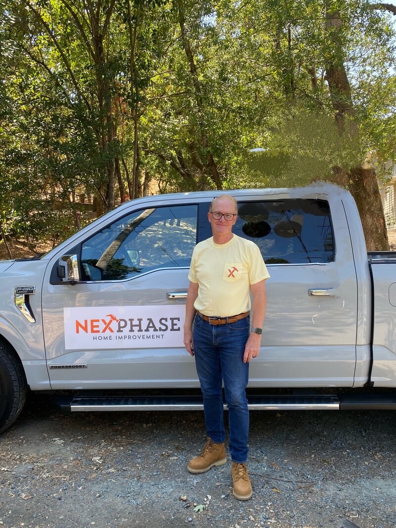 Scott Lohman, contractor and owner of NexPhase Home Improvement, standing beside a branded NexPhase Home Improvement work truck in a wooded East Bay neighborhood.