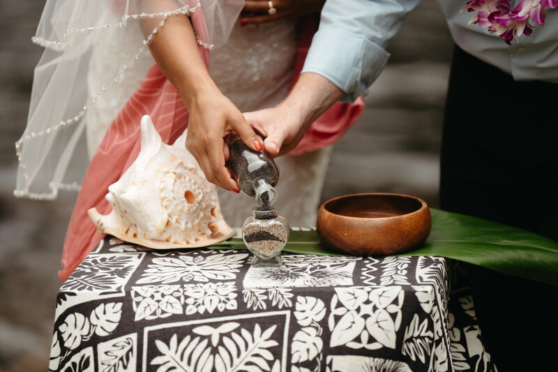 Close-up photo of a couple pouring sand from a jar into another jar in their elopement ceremony