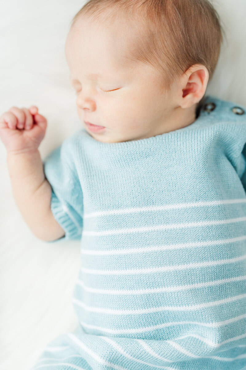 Newborn baby peacefully sleeping on their back, dressed in blue, with a serene expression