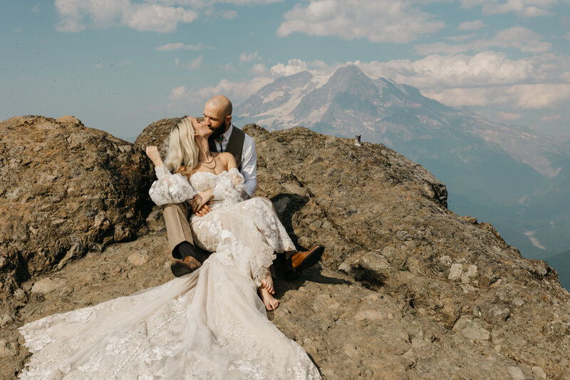 bride and groom sitting on a rock in front of a mountain