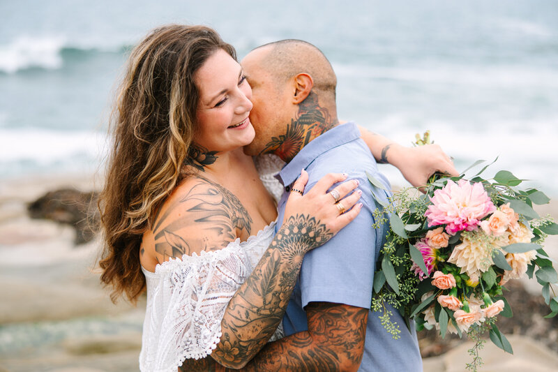 tattooed bride and groom kiss on the beach