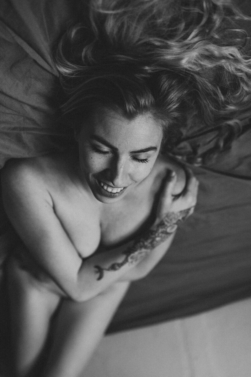 Black and White photo of a woman laying down on the bed, smiling