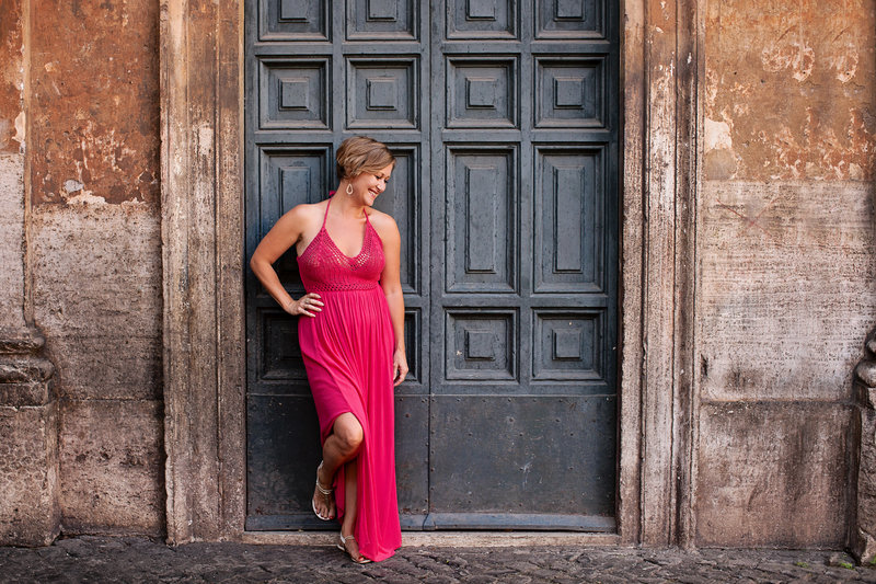 A beautiful girl in a pink dress in front of a slate blue roman door in Trastevere. Taken by Rome Solo Travel Photographer, Tricia Anne Photography