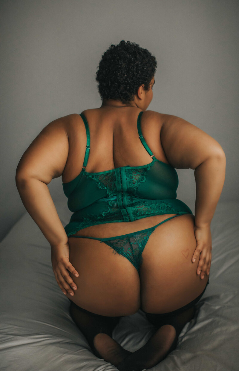 curvy boudoir model posing in green lingerie on bed