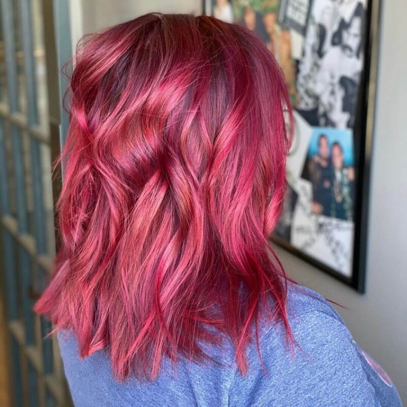 A woman with vibrant, wavy pink hair, showcasing a bold and stylish look created by 212 Salon, Spa, & Barbershop.