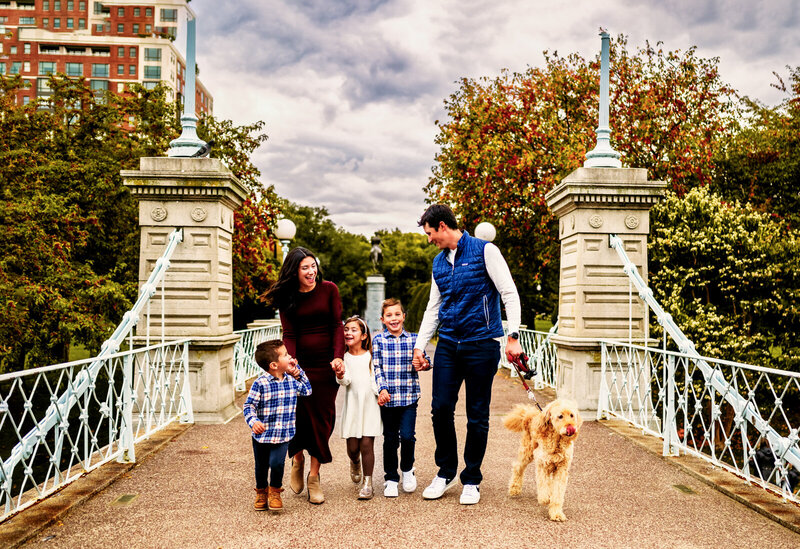 Family and dog holding hands while walking across a bridge in the Boston Public Garden.