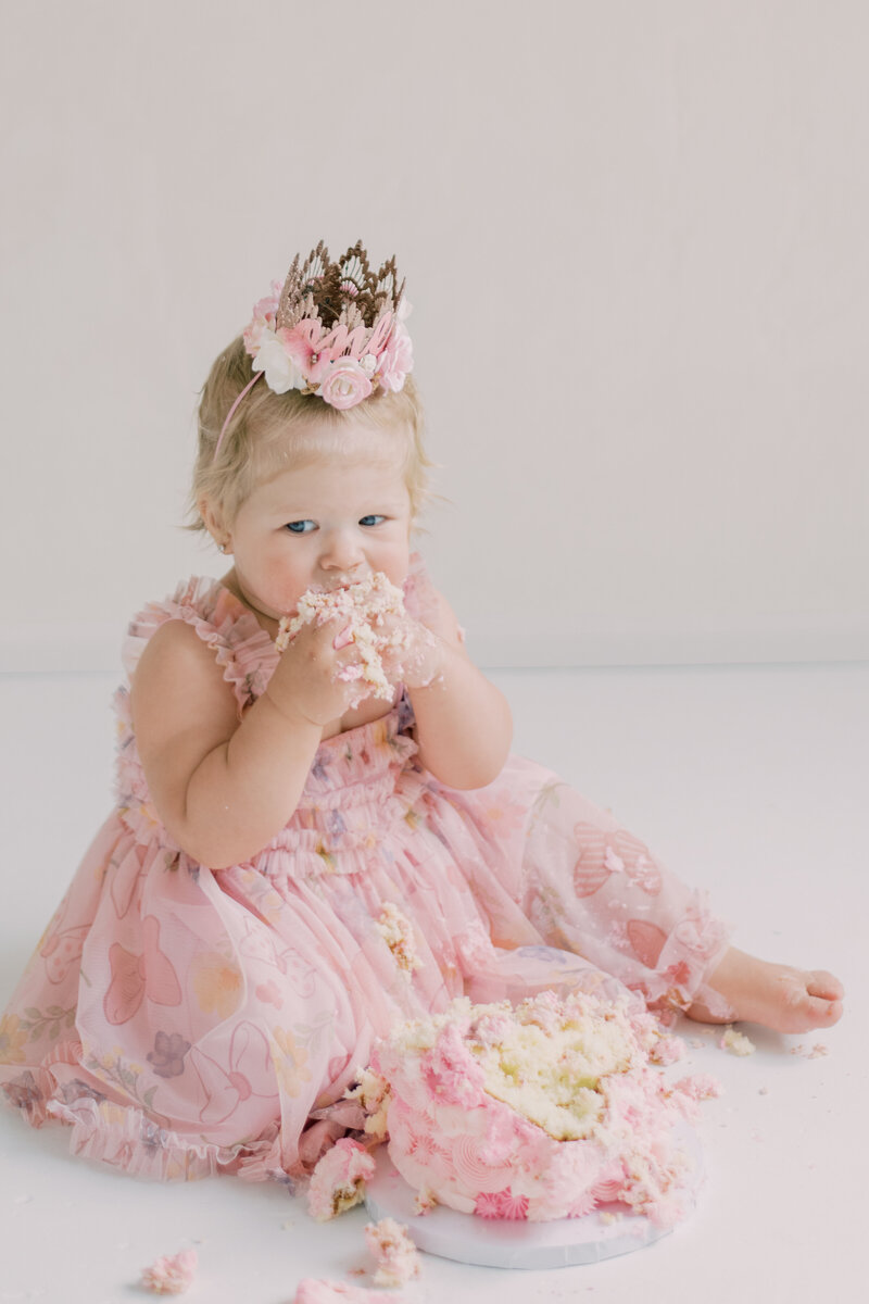 Little girl eating her birthday cake in Burlington Ontario, dressed in pink with a crown on her head