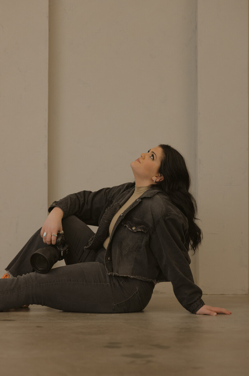 Brigette holding her camera and looking slightly over her shoulder at the camera, holding a neutral face.