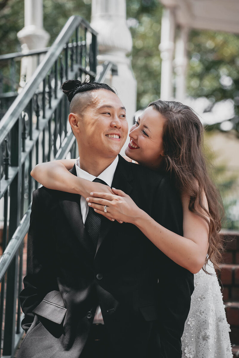 bride embracing groom from behind while they both smile