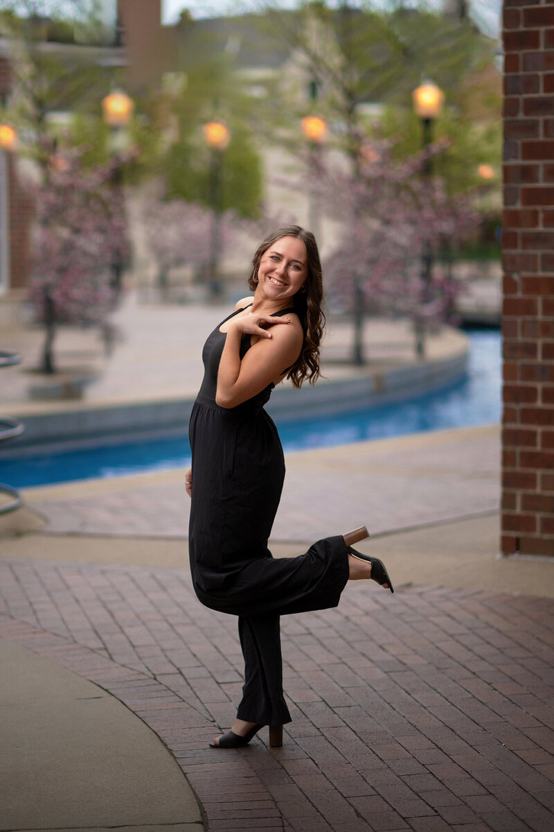 A happy high school grad in a black jumper poses with a leg up behind her taken by an Iowa Senior Photographer