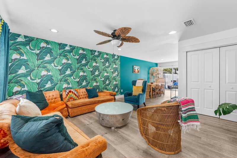 Spacious living area with bold banana leaf wallpaper, velvet sectional seating, and boho-chic decor in Panama City Beach rental.