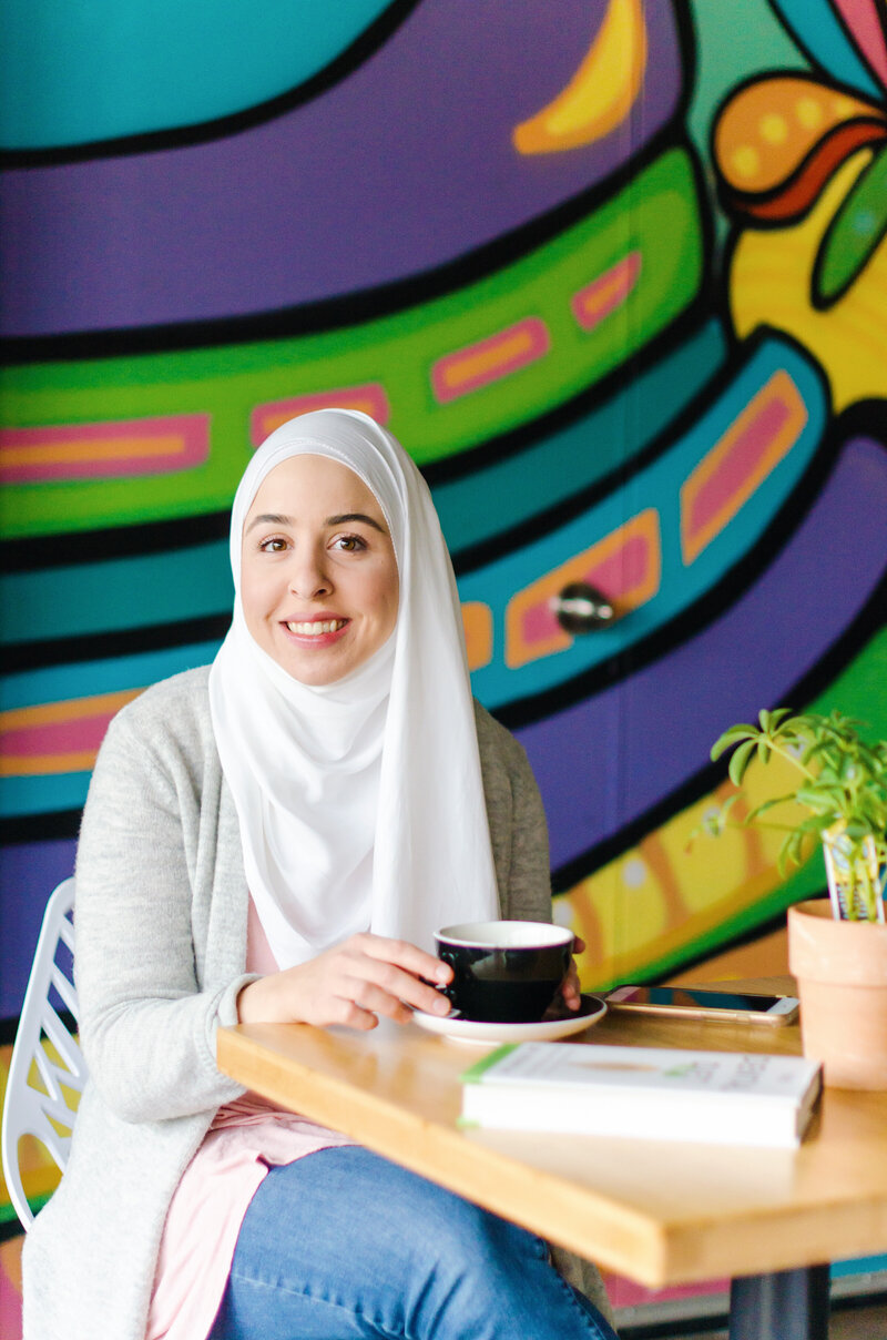 Fitness hijabi coach Hanan posing with a smile and a cup of tea with a colorful background
